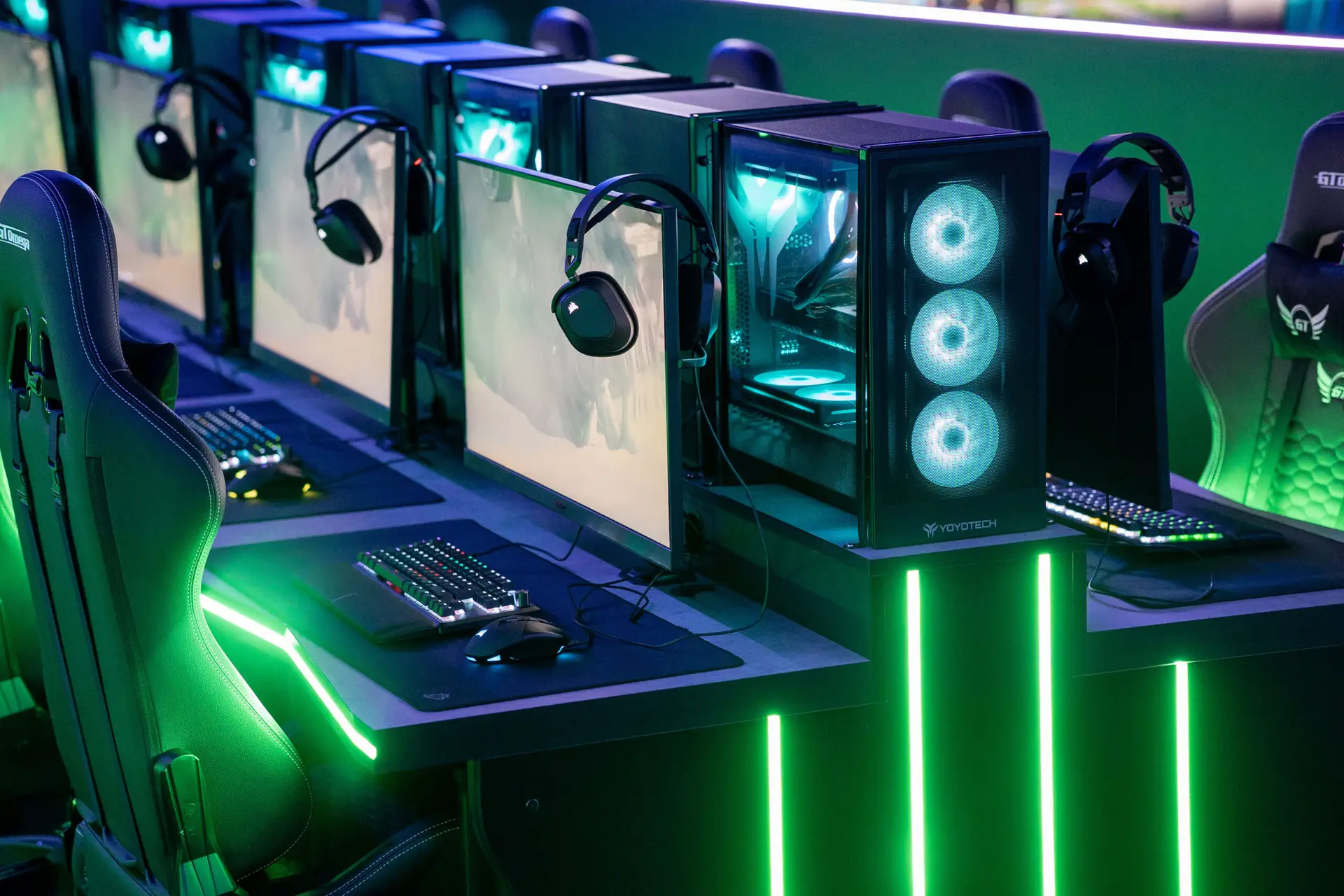 Row of high-spec gaming PCs with green LED lighting in a modern school esports arena design