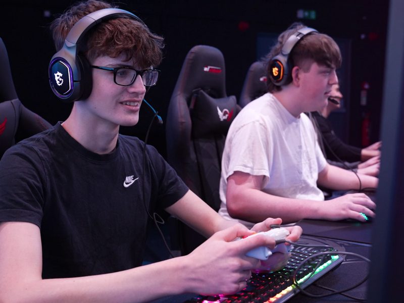 Students actively engaged in esports education and teamwork using headsets and controllers inside a Yoyotech educational esports arena.